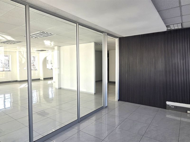 Modern open-plan office space featuring glass partitions, sleek tiled flooring, and contemporary fluted wall paneling, offering a bright and professional work environment.