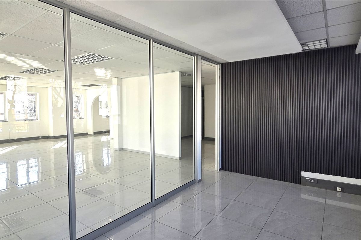 Modern open-plan office space featuring glass partitions, sleek tiled flooring, and contemporary fluted wall paneling, offering a bright and professional work environment.