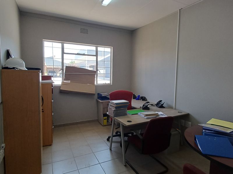 A functional office space featuring tiled flooring, a wall-mounted whiteboard, and a window with security bars, providing a practical work environment.