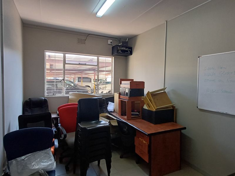 A functional office space featuring a wall-mounted whiteboard, fluorescent lighting, and an aluminium-framed window overlooking the parking area.