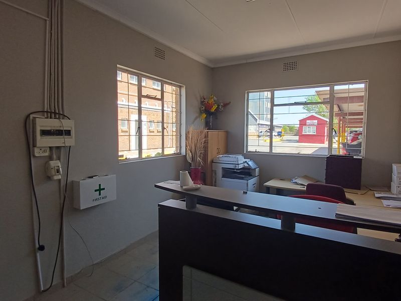 A functional office space featuring tiled flooring, steel-framed windows, and a wall-mounted electrical distribution board.