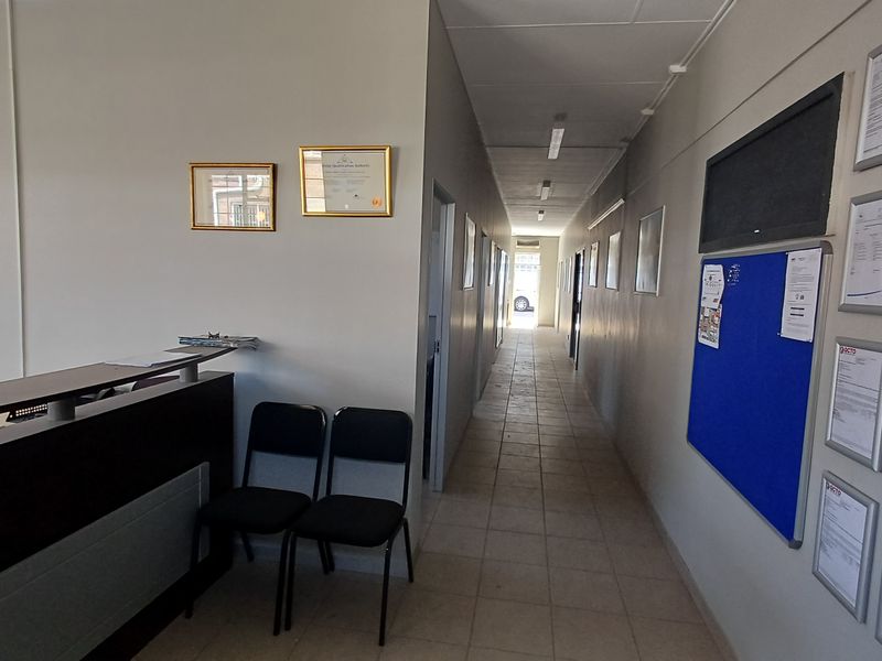 Office hallway featuring tiled flooring, fluorescent lighting, and a reception desk area leading to multiple office doors.