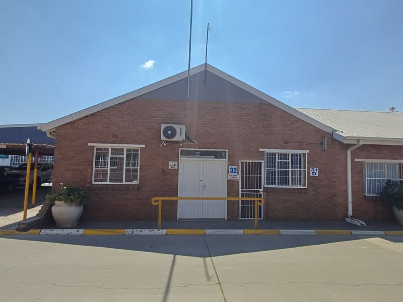 Front exterior view of a brick office building featuring a paved driveway, security bars on windows, and an external air conditioning unit.