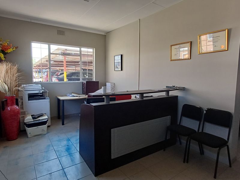 A functional office reception area featuring tiled flooring, aluminum windows, and a built-in reception desk, suitable for professional business operations.