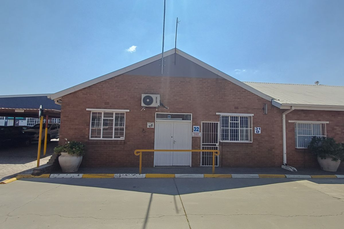 Front exterior view of a brick office building featuring a paved driveway, security bars on windows, and an external air conditioning unit.
