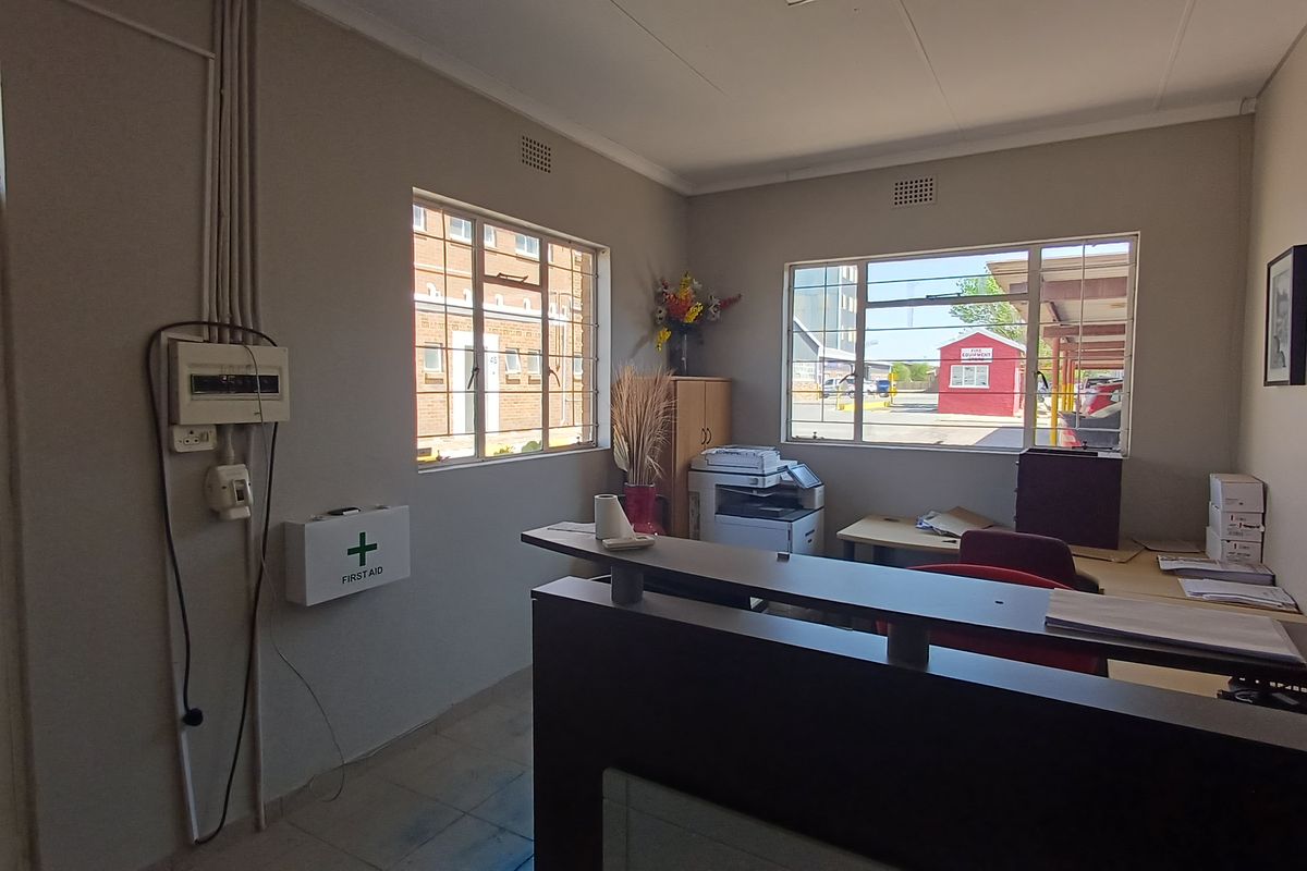 A functional office space featuring tiled flooring, steel-framed windows, and a wall-mounted electrical distribution board.
