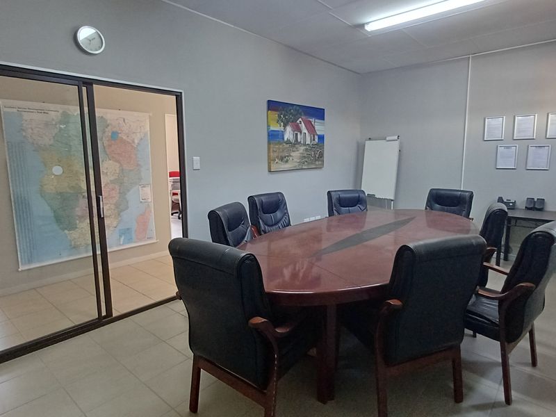 A functional office boardroom featuring tiled flooring, fluorescent lighting, and a sliding glass door providing access to an adjacent workspace.