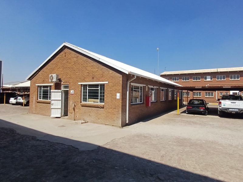 Exterior view of a single-story face brick office building featuring a gabled roof, steel-framed windows, and an adjacent paved parking area.