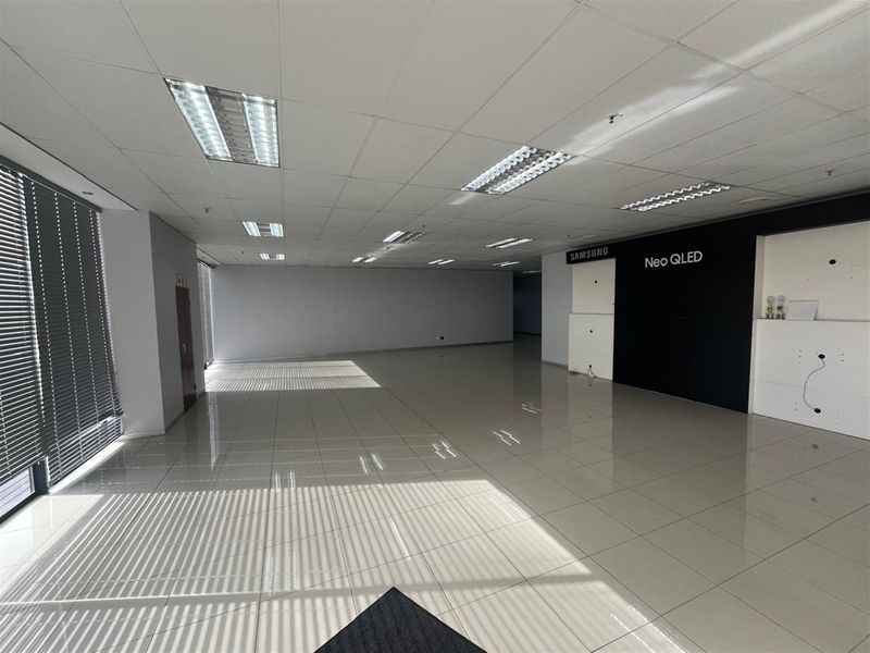 Spacious open-plan office area featuring tiled flooring, suspended ceilings with recessed lighting, and large windows with fitted blinds.