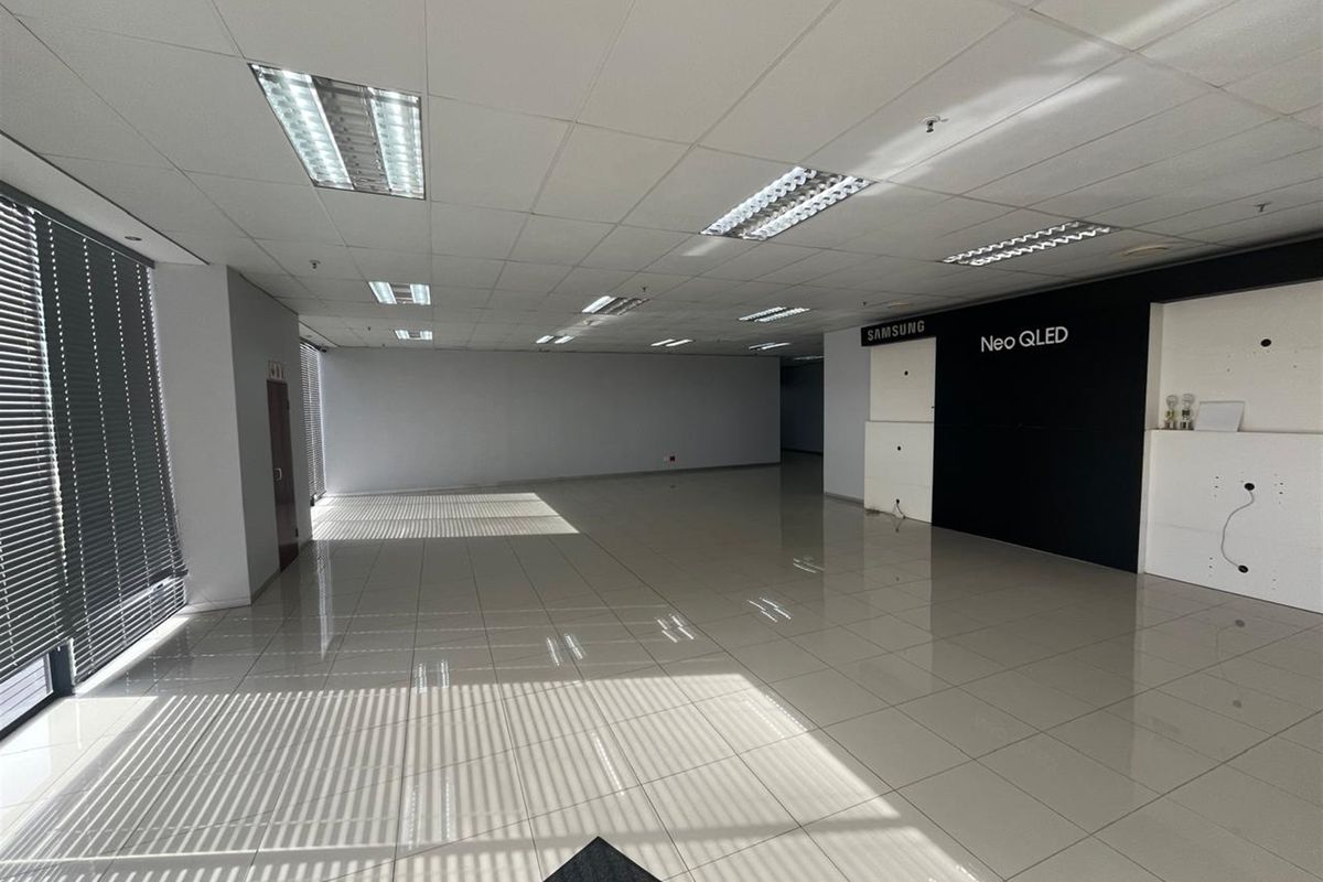 Spacious open-plan office area featuring tiled flooring, suspended ceilings with recessed lighting, and large windows with fitted blinds.