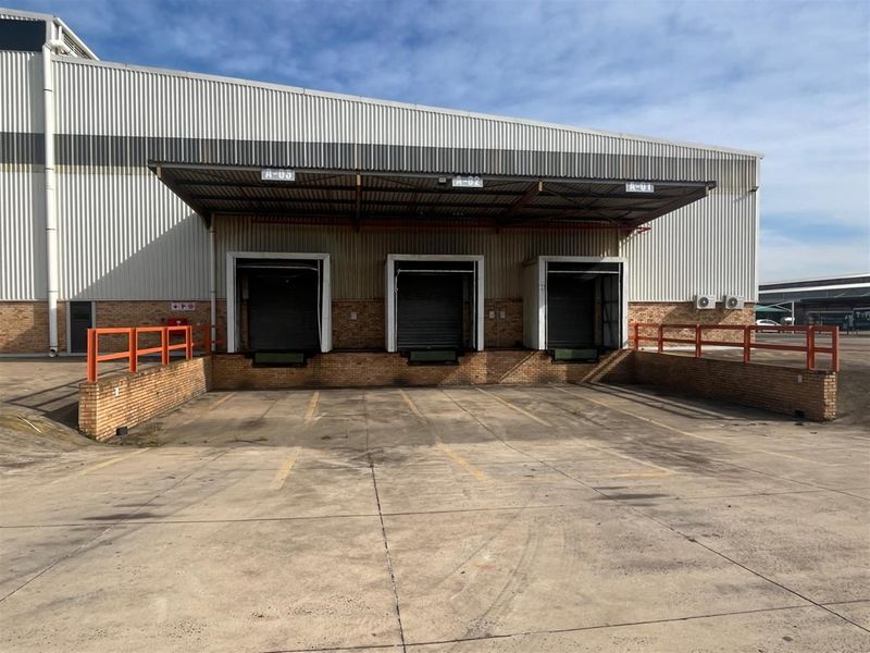 Industrial warehouse exterior featuring three loading docks with roller shutter doors, a protective metal canopy, and a concrete yard area.