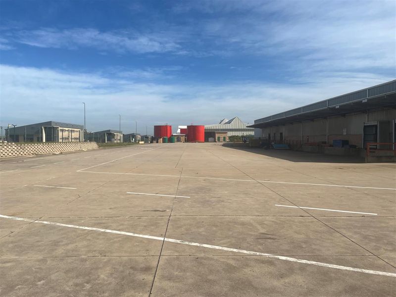 Expansive industrial concrete yard featuring a large warehouse facility with loading bay canopy and prominent storage tanks.