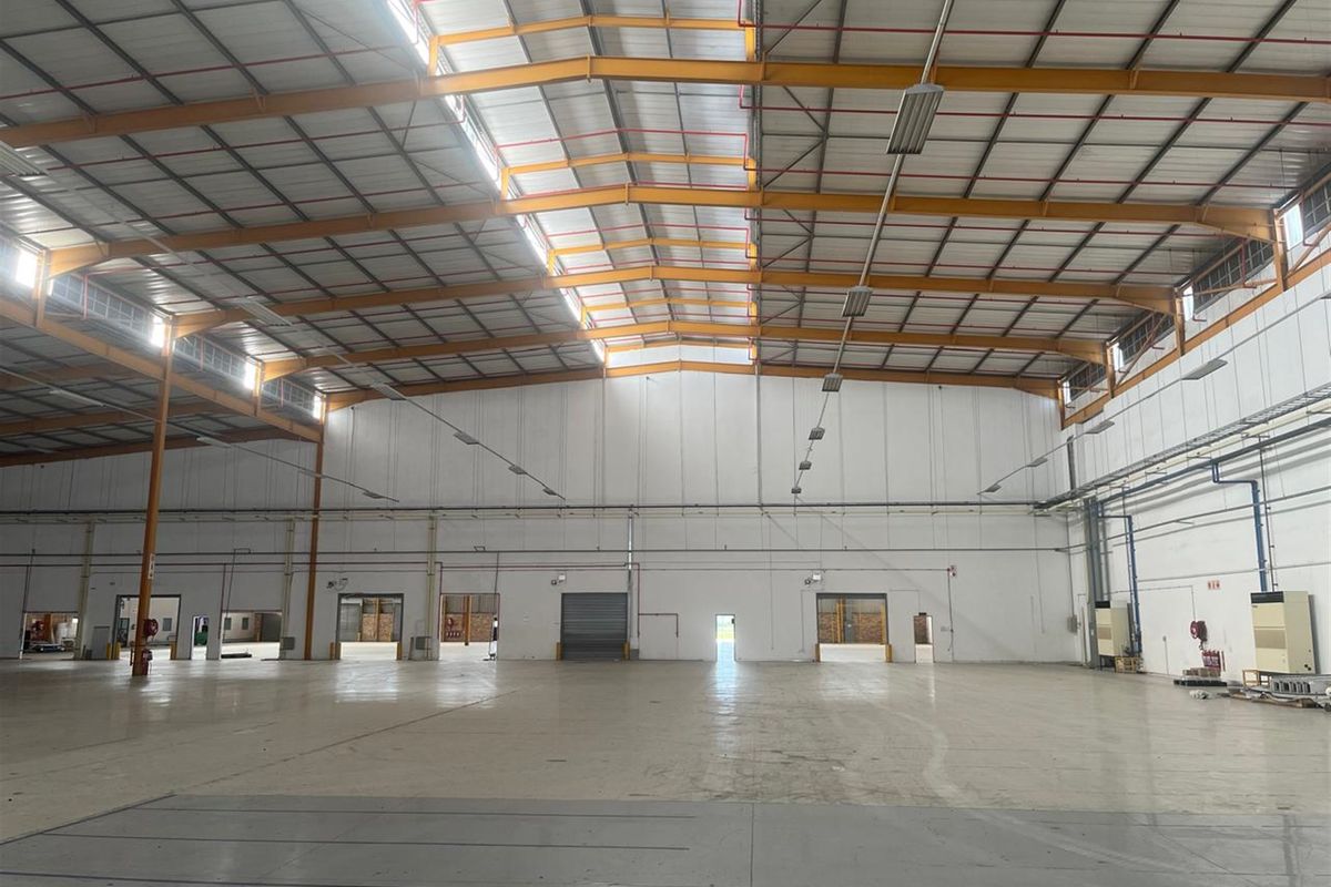 Spacious industrial warehouse featuring high ceilings, steel portal frame construction, concrete flooring, multiple roller shutter access points, and integrated fire sprinkler system.