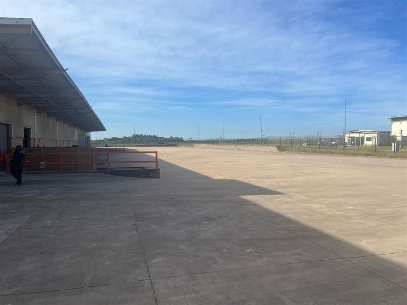 Expansive industrial concrete yard featuring a covered loading dock area, perimeter fencing, and ample space for logistics and vehicle maneuvering.
