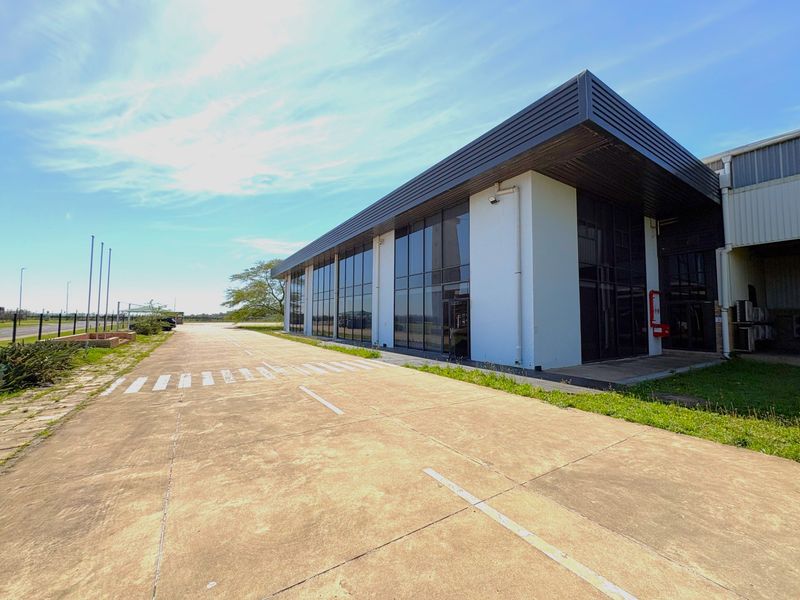 Modern industrial building facade featuring extensive glass curtain walling and a concrete driveway approach.