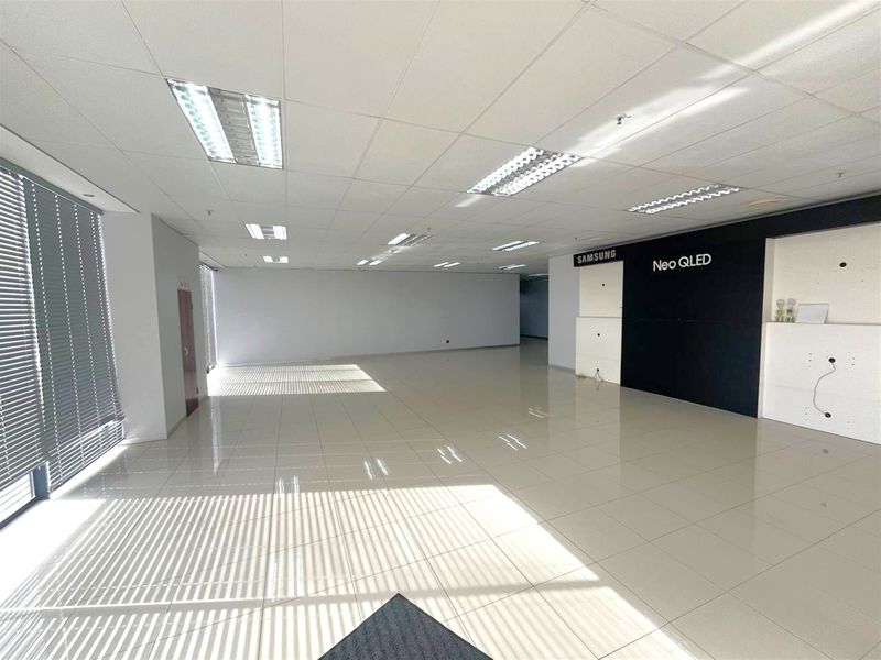 Spacious open-plan industrial office or showroom area featuring polished ceramic floor tiles, suspended ceiling with recessed lighting, and large windows with fitted venetian blinds.