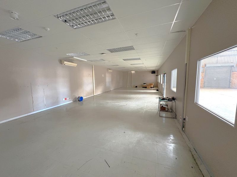 Spacious open-plan industrial office area featuring epoxy flooring, suspended ceilings with recessed lighting, and wall-mounted air conditioning units.