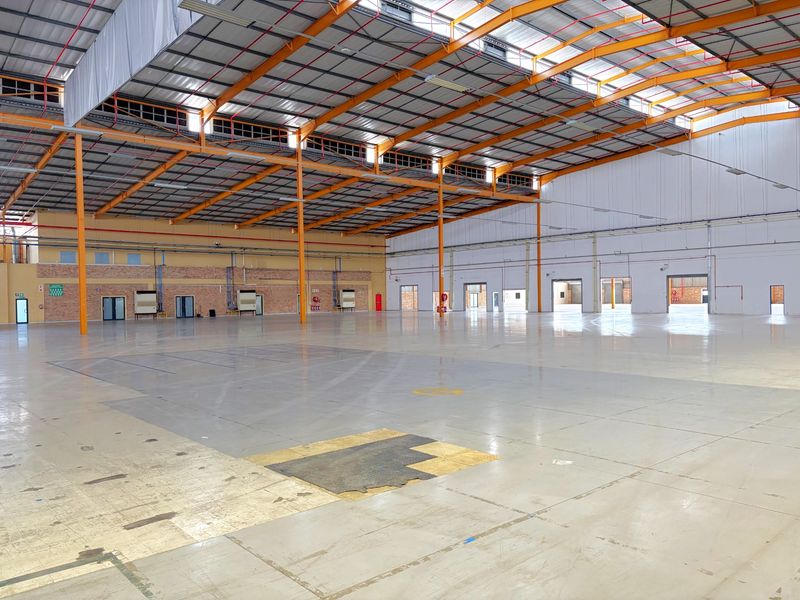 Spacious industrial warehouse featuring high ceilings with exposed steel trusses, durable epoxy flooring, and multiple access points for efficient logistics and operations.