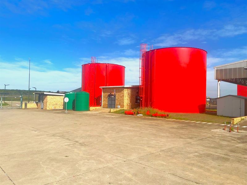Industrial yard featuring large red storage tanks, a brick utility building, and a concrete surface area.