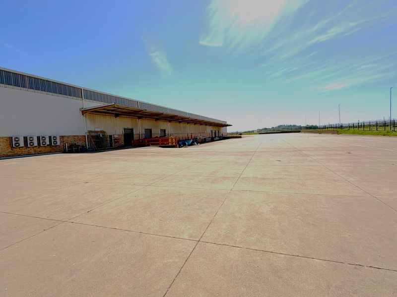 Expansive concrete yard area adjacent to an industrial warehouse building featuring metal cladding and a loading canopy.