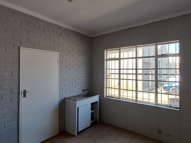 A functional office kitchenette featuring a sink, built-in cabinetry, and security bars on the window, providing a practical space for staff amenities.
