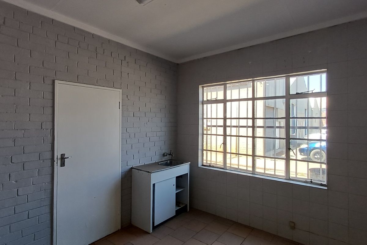 A functional office kitchenette featuring a sink, built-in cabinetry, and security bars on the window, providing a practical space for staff amenities.