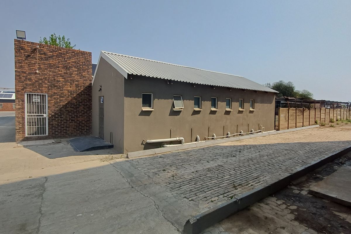 Exterior view of a commercial office building featuring a brick section, plastered walls, metal roofing, and paved access area.