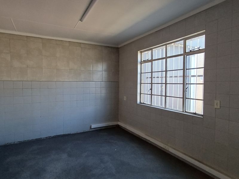 An empty office space featuring tiled walls, a window with security bars, and basic electrical infrastructure, ready for customization.