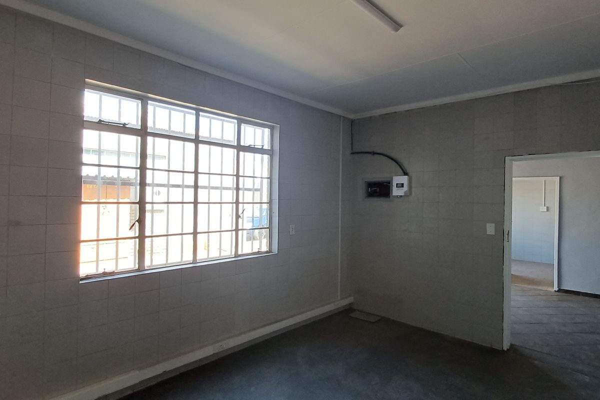 An empty office space featuring tiled walls, security bars on the window, and an exposed electrical distribution board.