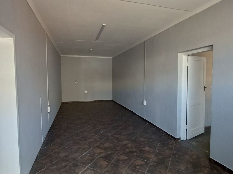 An empty office space featuring tiled flooring, neutral grey walls, and surface-mounted electrical conduits, providing a clean and functional workspace.