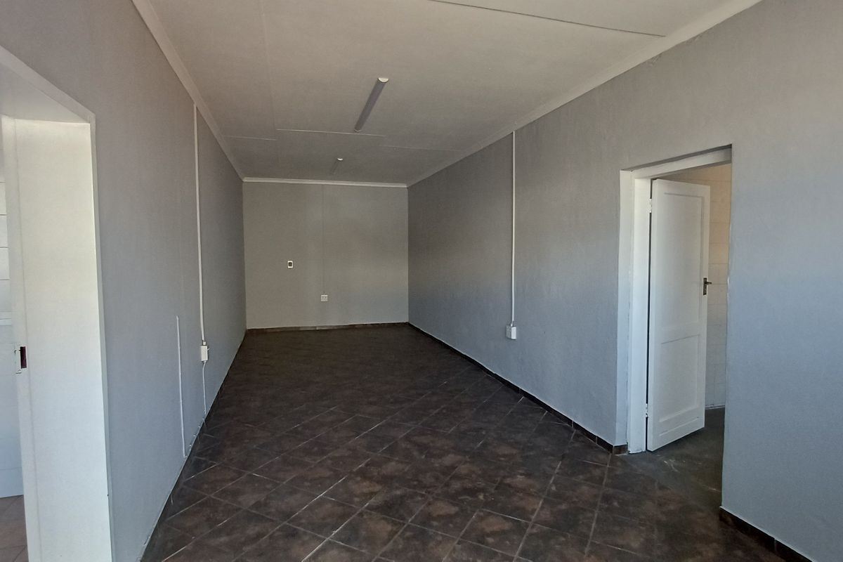 An empty office space featuring tiled flooring, neutral grey walls, and surface-mounted electrical conduits, providing a clean and functional workspace.