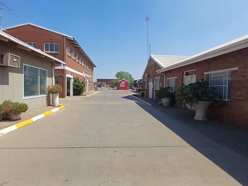 Exterior view of an office complex featuring brick buildings, concrete driveway, and security-fitted windows under a clear sky.