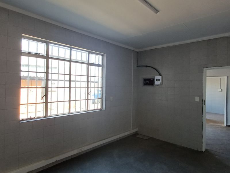 An empty office space featuring tiled walls, security bars on the window, and an exposed electrical distribution board.
