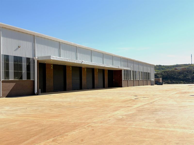 Industrial warehouse exterior featuring multiple roller shutter doors, a covered loading bay, and a large concrete yard area.