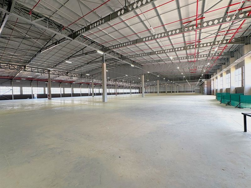Expansive industrial warehouse space featuring high ceilings with exposed steel trusses, fire sprinkler systems, and durable concrete flooring throughout.