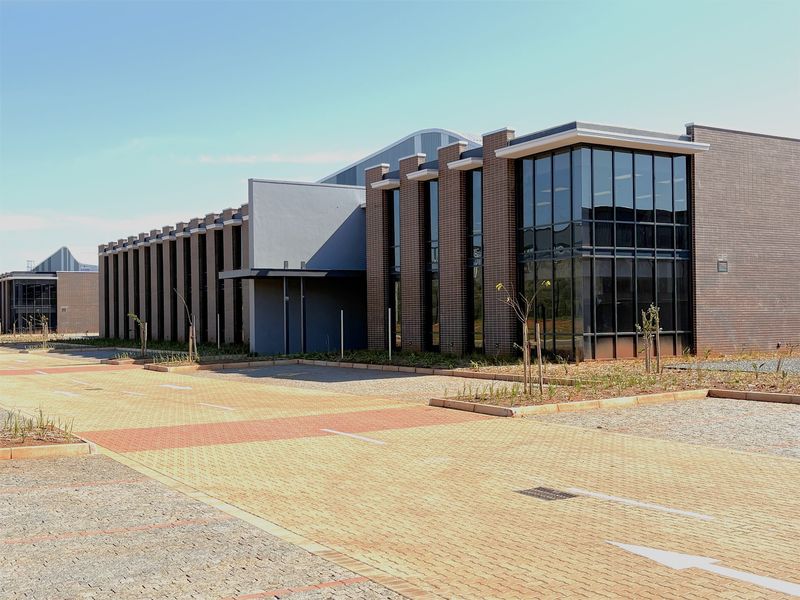 Modern industrial building featuring a brick facade, extensive glass curtain walling, and a paved parking area with landscaped surroundings.
