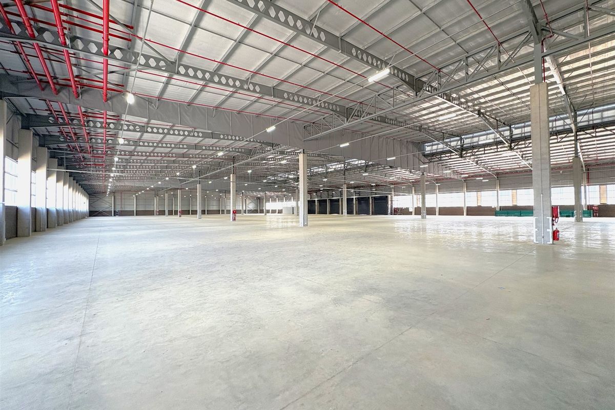 Expansive industrial warehouse space featuring high ceilings with exposed steel trusses, polished concrete flooring, and a comprehensive fire sprinkler system.