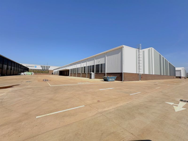Large industrial warehouse facility featuring metal cladding, a brick base, and an expansive concrete yard area suitable for logistics and heavy vehicle access.