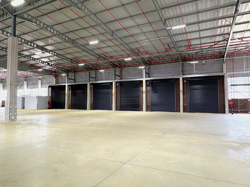 Spacious industrial warehouse featuring high ceilings, concrete flooring, fire sprinkler system, and multiple roller shutter doors for efficient loading and access.