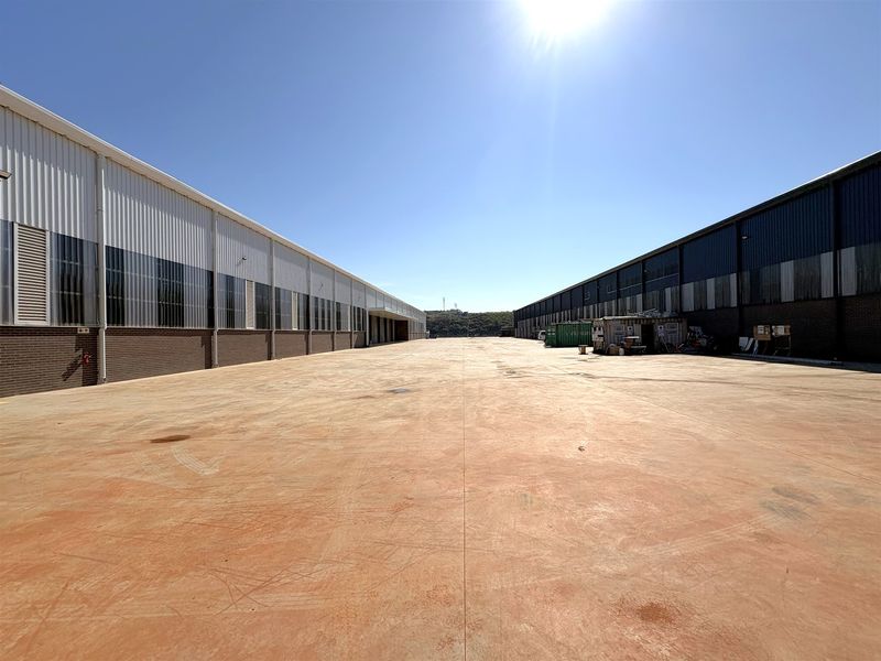 Expansive industrial concrete yard situated between two large warehouse structures with metal cladding and brick facade finishes.