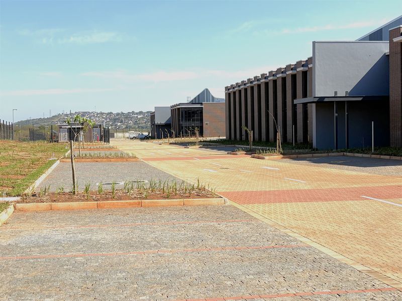 A view of the industrial property exterior featuring a paved driveway, landscaped garden beds, and modern building facades.