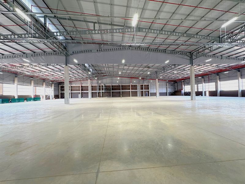 A large, open-plan industrial warehouse space featuring a high steel portal frame, polished concrete flooring, and an integrated fire sprinkler system.
