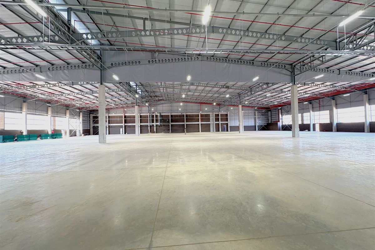 A large, open-plan industrial warehouse space featuring a high steel portal frame, polished concrete flooring, and an integrated fire sprinkler system.