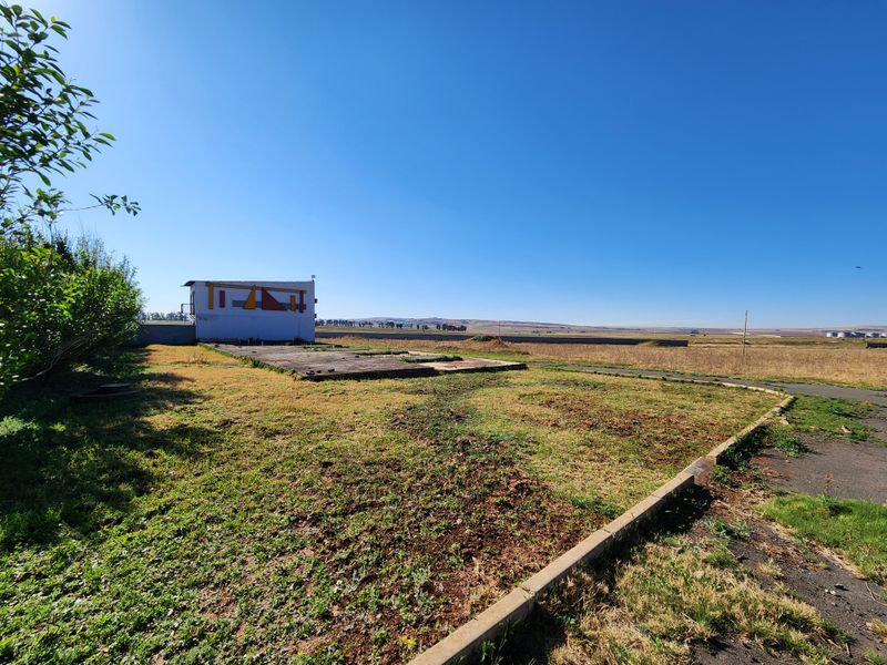 A view of a vacant commercial plot featuring a concrete slab foundation, paved curbing, and a small utility structure set against an open landscape.