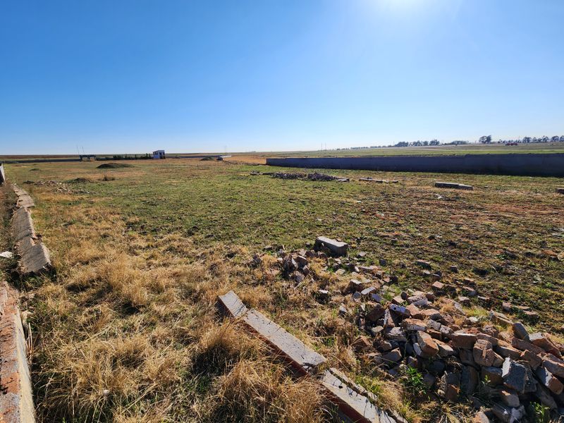 A wide-angle view of a vacant commercial plot featuring a concrete boundary wall and scattered construction debris on the ground.