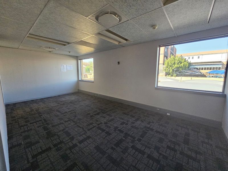 A vacant office space featuring carpet tiles, a suspended ceiling with recessed lighting, and large windows providing natural light.