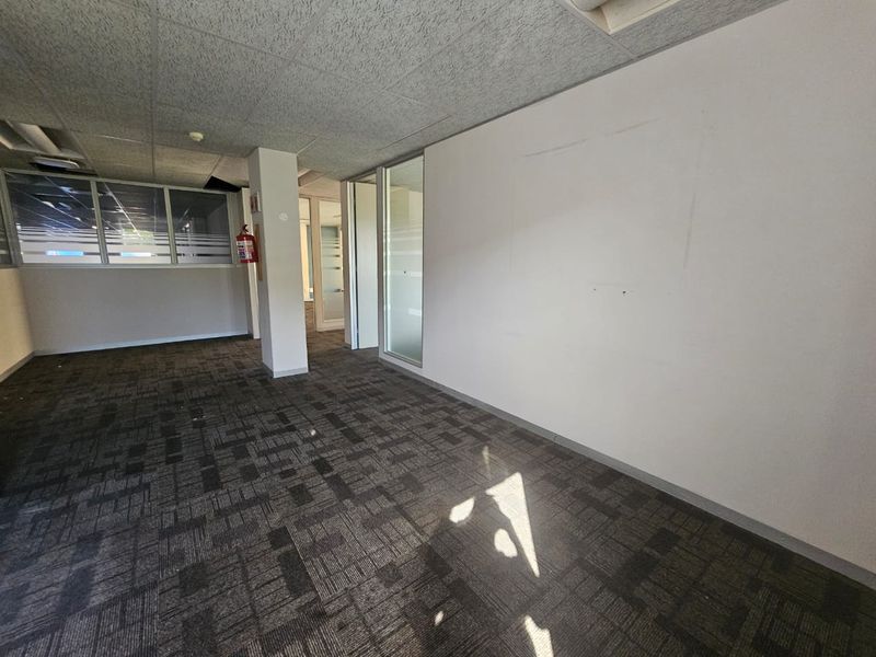 An empty office space featuring carpet tiles, suspended ceiling, and glass partition walls, suitable for a professional workspace setup.