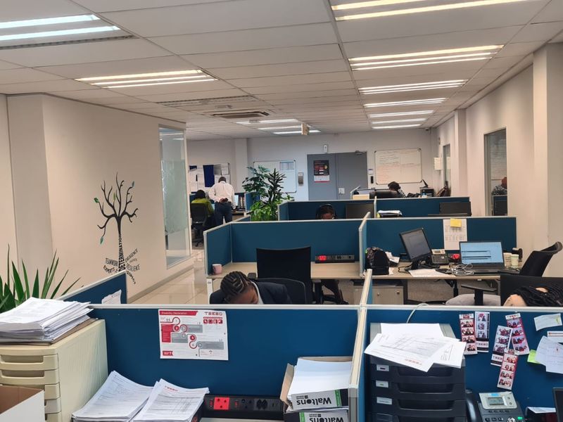 Open-plan office space featuring modular cubicle workstations, suspended ceiling with recessed lighting, and glass-partitioned office areas.