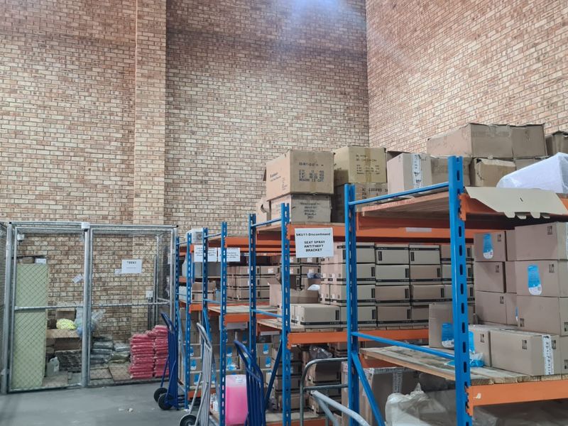 Industrial warehouse space featuring high exposed brick walls, concrete flooring, and heavy-duty steel shelving units for storage.
