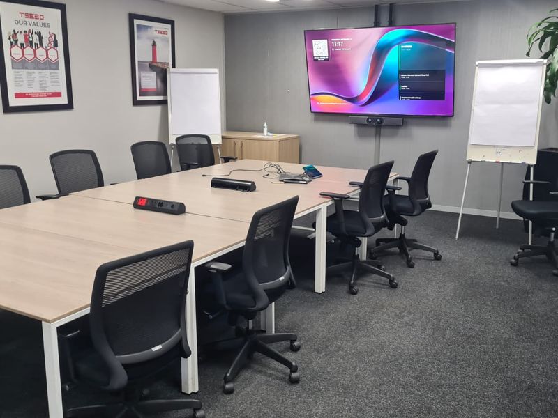 A professional boardroom or meeting room featuring a large wall-mounted display, integrated video conferencing technology, and neutral finishes.